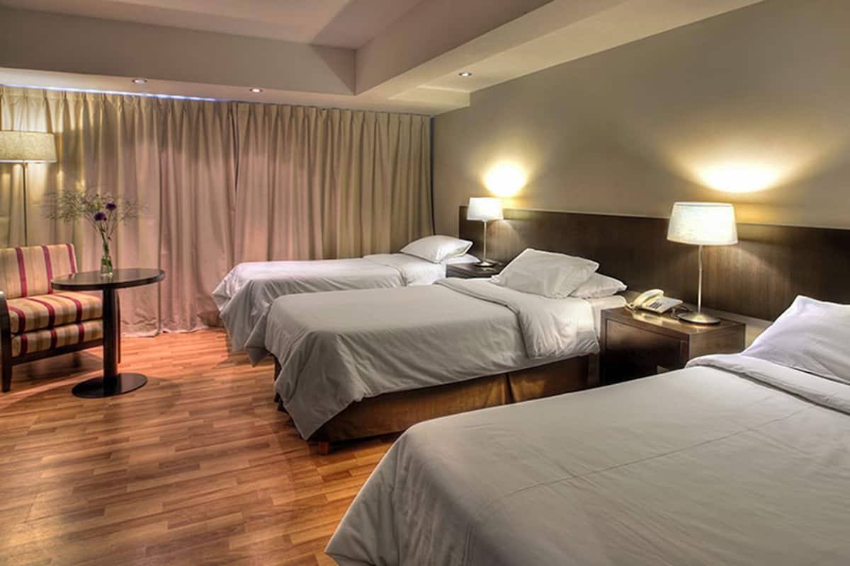 A hotel room with three beds, a desk, a chair, and two bedside lamps.