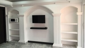 A hallway with a flat-screen TV mounted on a wall, flanked by white columns and arches. There are built-in shelves on either side of the TV. - Hostal Marlyn Sai (San Andrés)