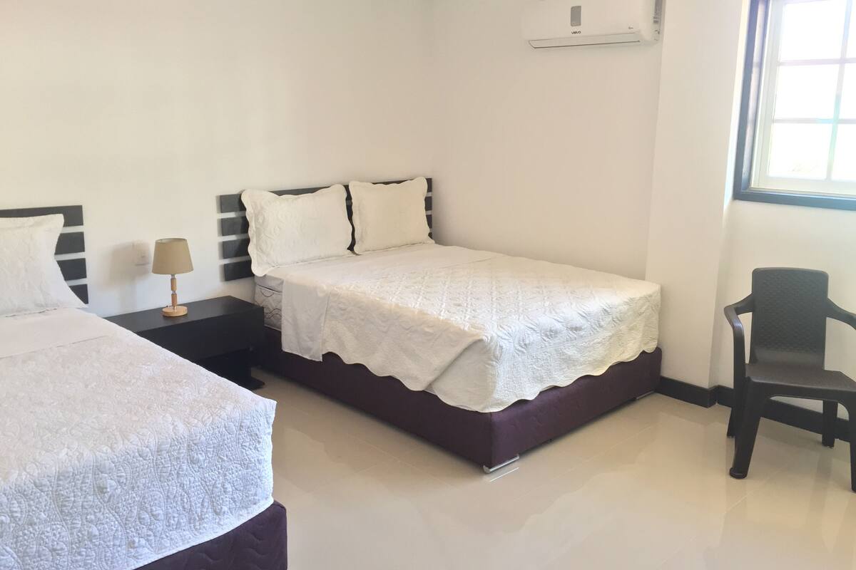 A hotel room with a bed, a chair, a nightstand, and a window.