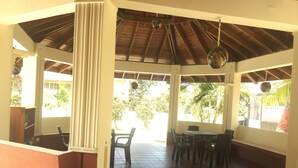 An open patio with a tiled floor, a table with chairs, and a ceiling with wooden beams and hanging decorations. - Hostal Marlyn Sai (San Andrés)