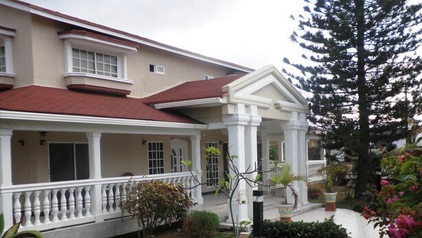 A two-story house with a covered porch, a red roof, and a well-maintained garden with various plants and a birdcage. - Hostal Marlyn Sai (San Andrés)