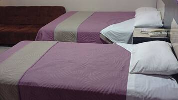 Duas camas de solteiro com roupa de cama roxa e branca, um sofá castanho e uma mesa de cabeceira com telefone.