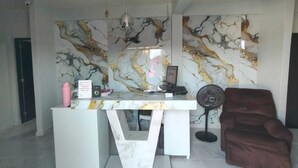 A modern reception desk with a marble wall, a laptop, a fan, and a brown armchair.