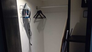 A small, dimly lit room with a white wall, a metal rack, and a hanging clothes rack.