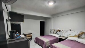 A hotel room with two beds, a desk, a chair, a TV, and a minibar.