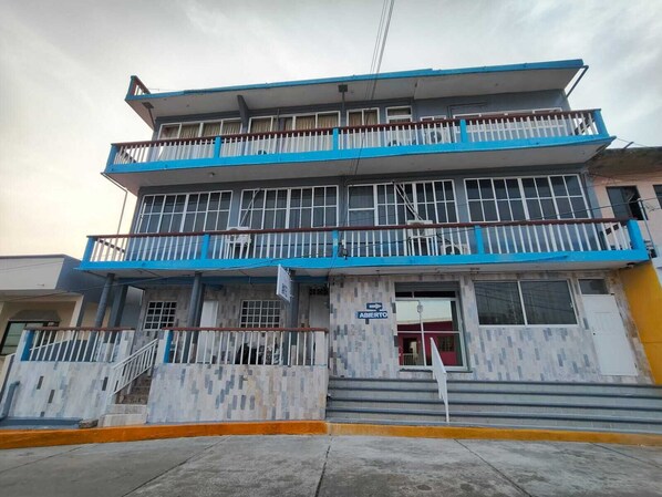 A multi-story building with a blue and white facade, a visible entrance with a sign, and a staircase leading to the entrance.