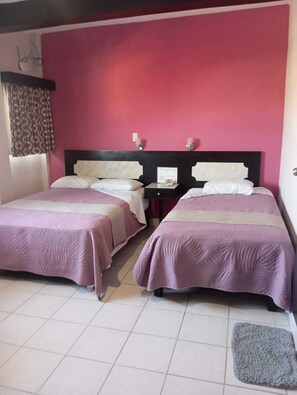 Two single beds with matching headboards and footboards, a bedside table, and a window with patterned curtains.