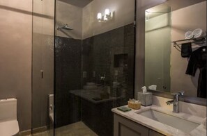 A modern bathroom with a glass-enclosed shower, a large mirror, and a sink with toiletries. - Demetria Bungalows (Guadalajara)