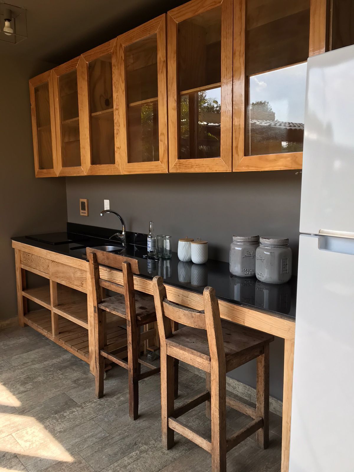 A kitchen with wooden cabinets, a black countertop, a refrigerator, and a dining area with chairs.