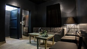 A dark-themed living room with a sofa, a coffee table, a lamp, and a door leading to another room.