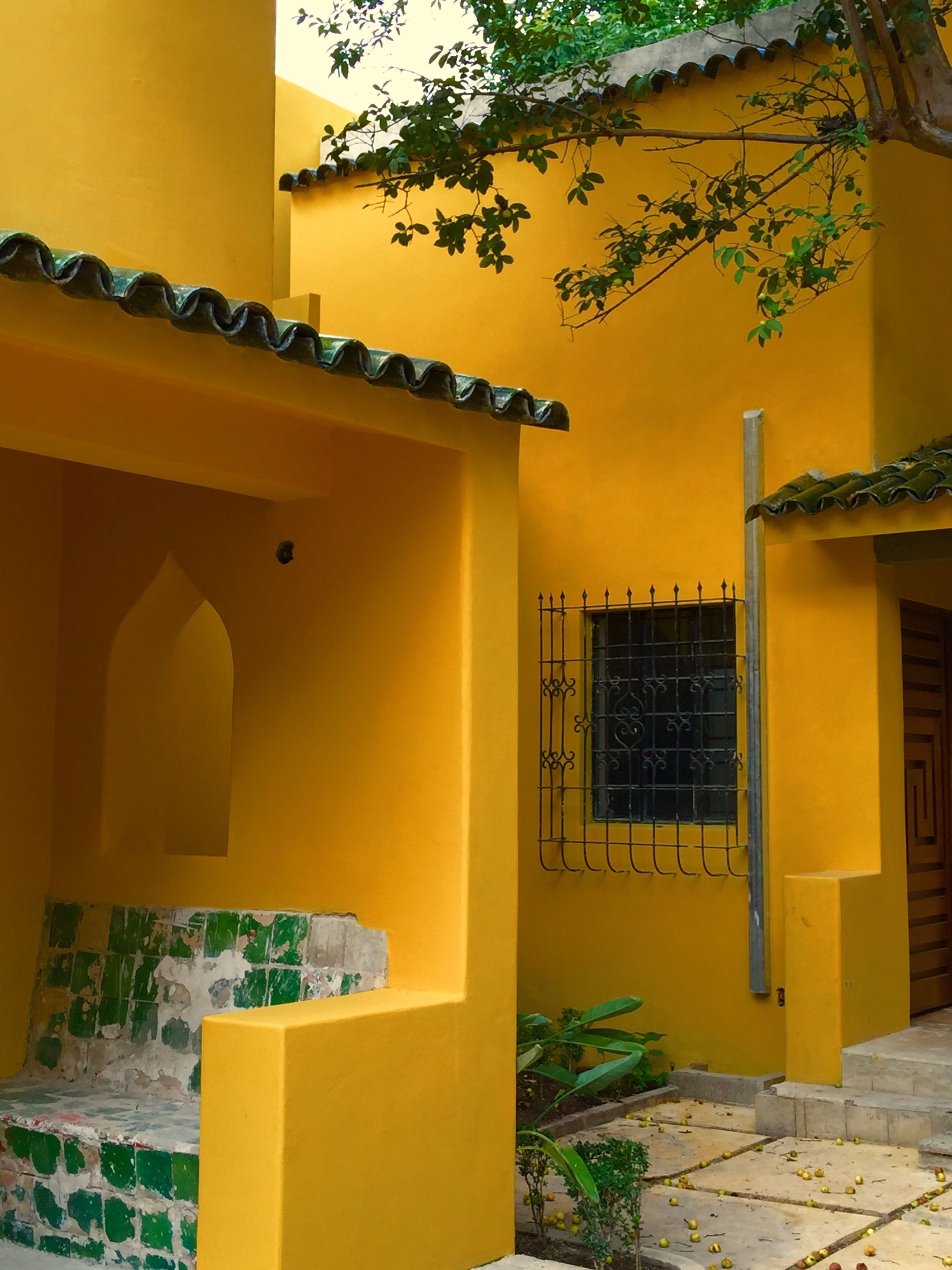 Un edificio amarillo con techo de tejas, una ventana con rejas de hierro decorativas y una motocicleta verde estacionada afuera.