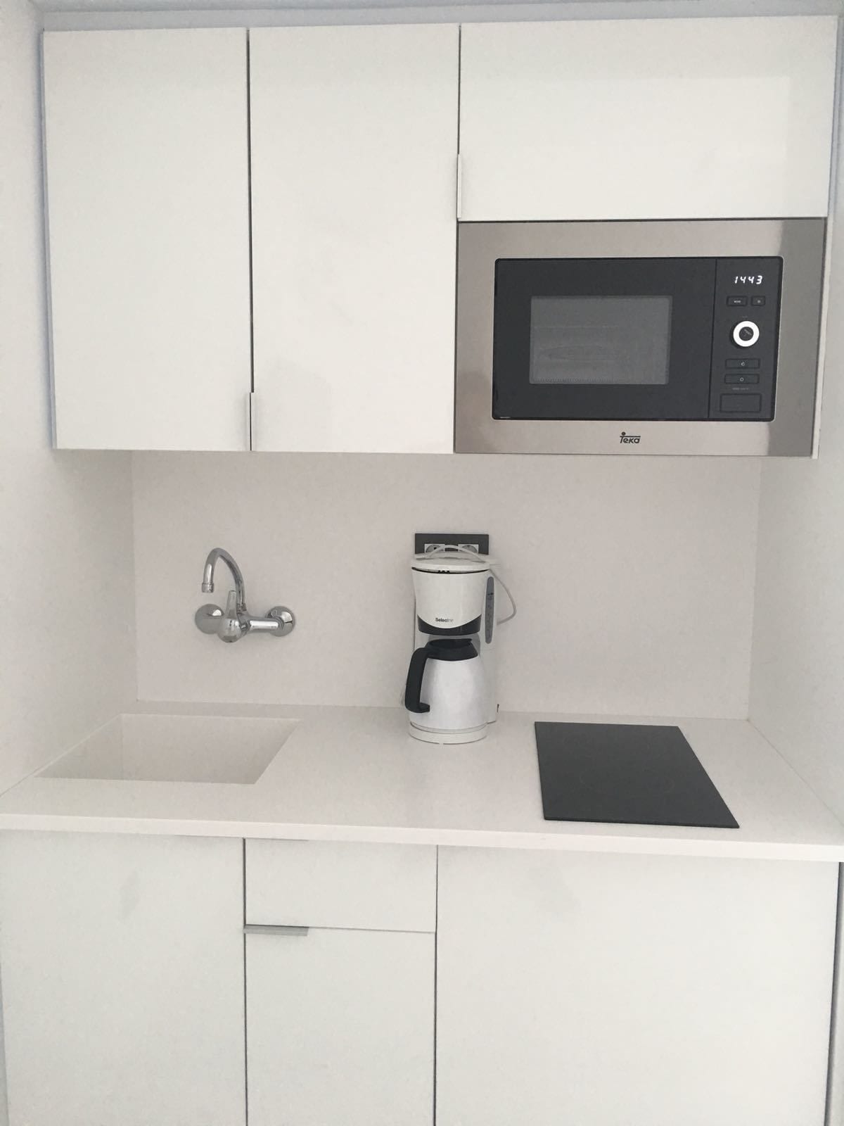 Una kitchenette compacta con microondas, cafetera y lavabo.