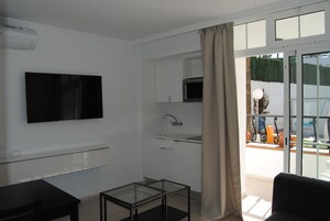 A modern living room with a flat-screen TV, a glass coffee table, a sofa, and a sliding glass door leading to an outdoor area.