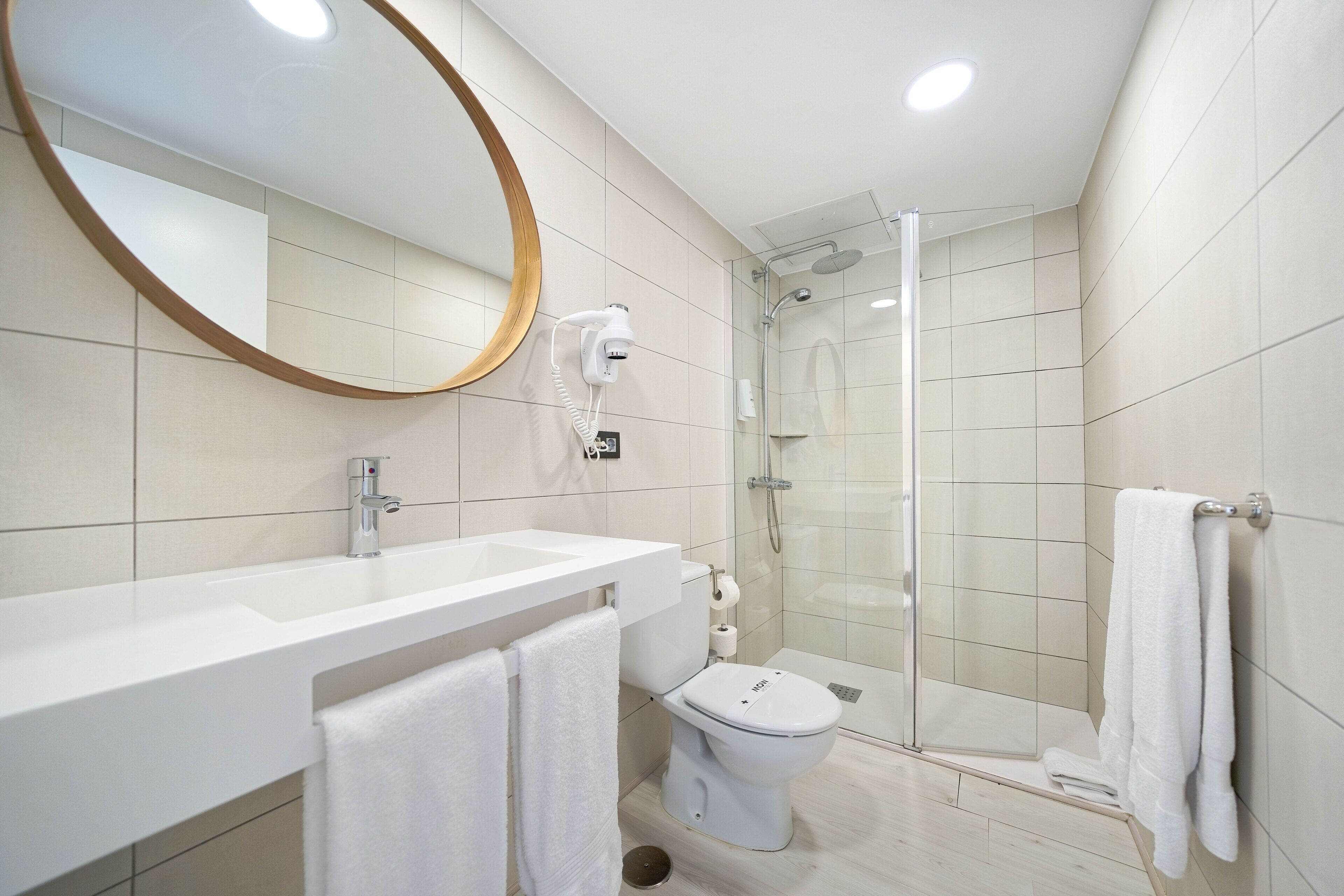 Une salle de bain moderne avec un lavabo blanc, des toilettes, une douche et un grand miroir.