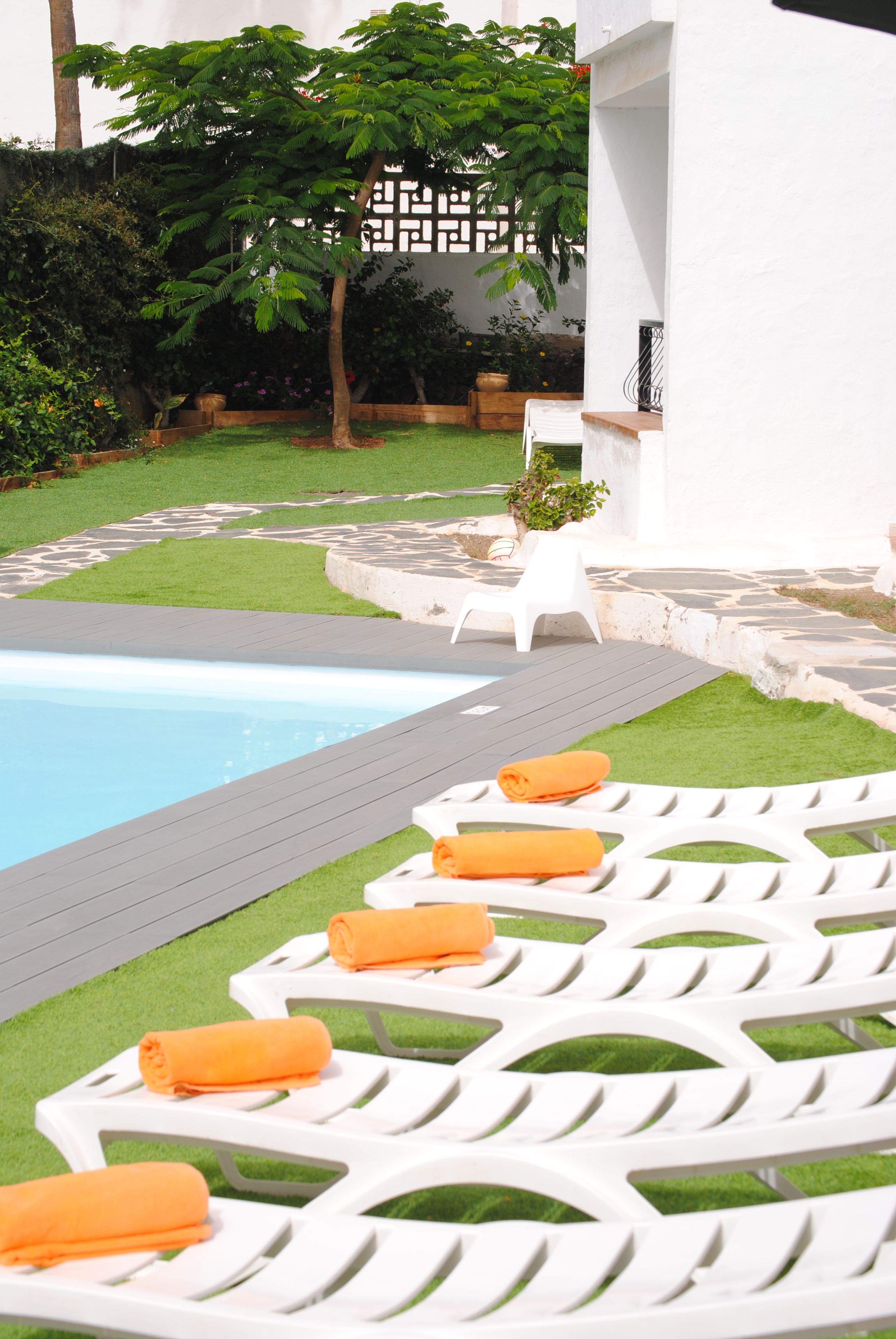 Ein Poolbereich mit weißen Liegestühlen und orangefarbenen Handtüchern, umgeben von einer gepflegten Rasenfläche und einem Steinweg.
