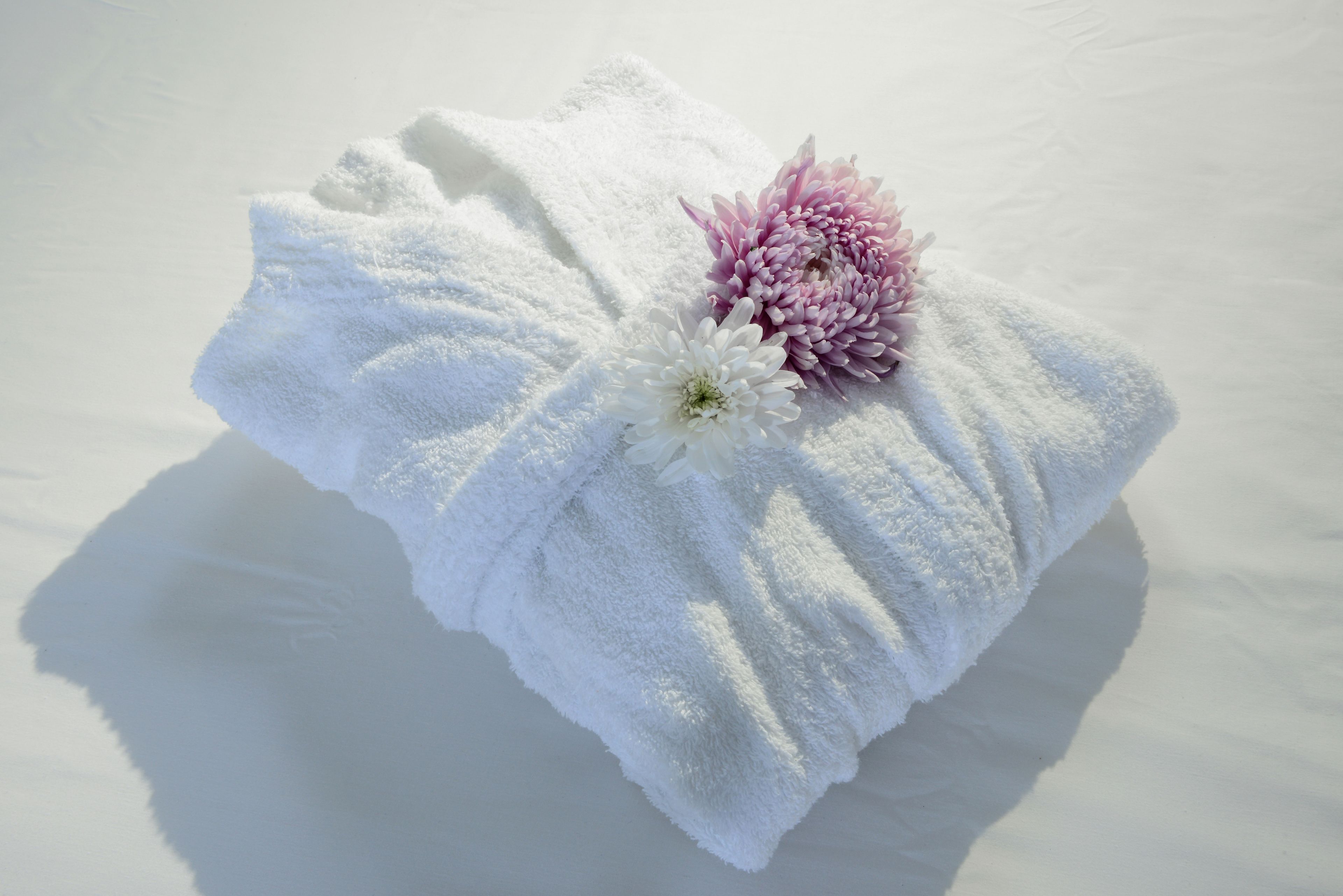 A white towel with a pink flower and a white flower on a white surface.