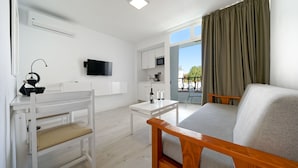Una habitación moderna y bien iluminada con un escritorio blanco, un banco de madera, un sofá y un televisor.