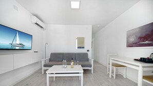 Una sala de estar moderna y minimalista con un sofá blanco, una mesa de centro blanca y un televisor de pantalla plana montado en la pared.