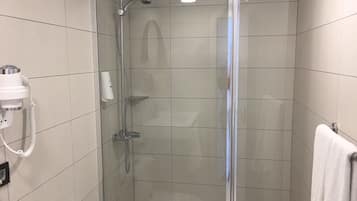 Eine begehbare Glasdusche mit Handbrause, Fön und Handtuchhalter.