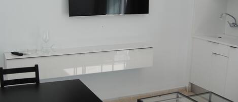 Una cocina moderna con armarios blancos, lavavajillas incorporado y televisor de pantalla plana montado en la pared.