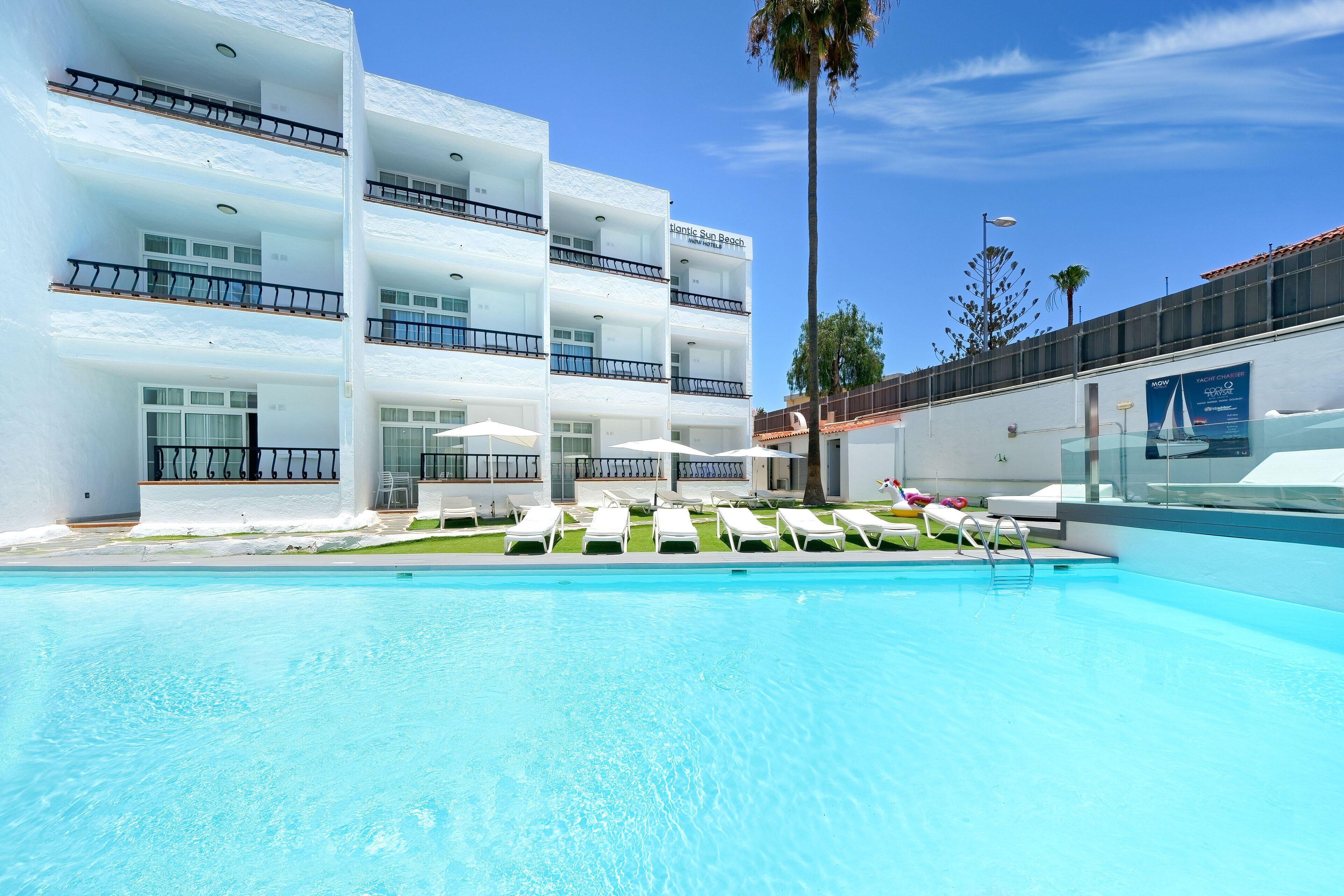 A hotel with a swimming pool, multiple balconies, and sun loungers.