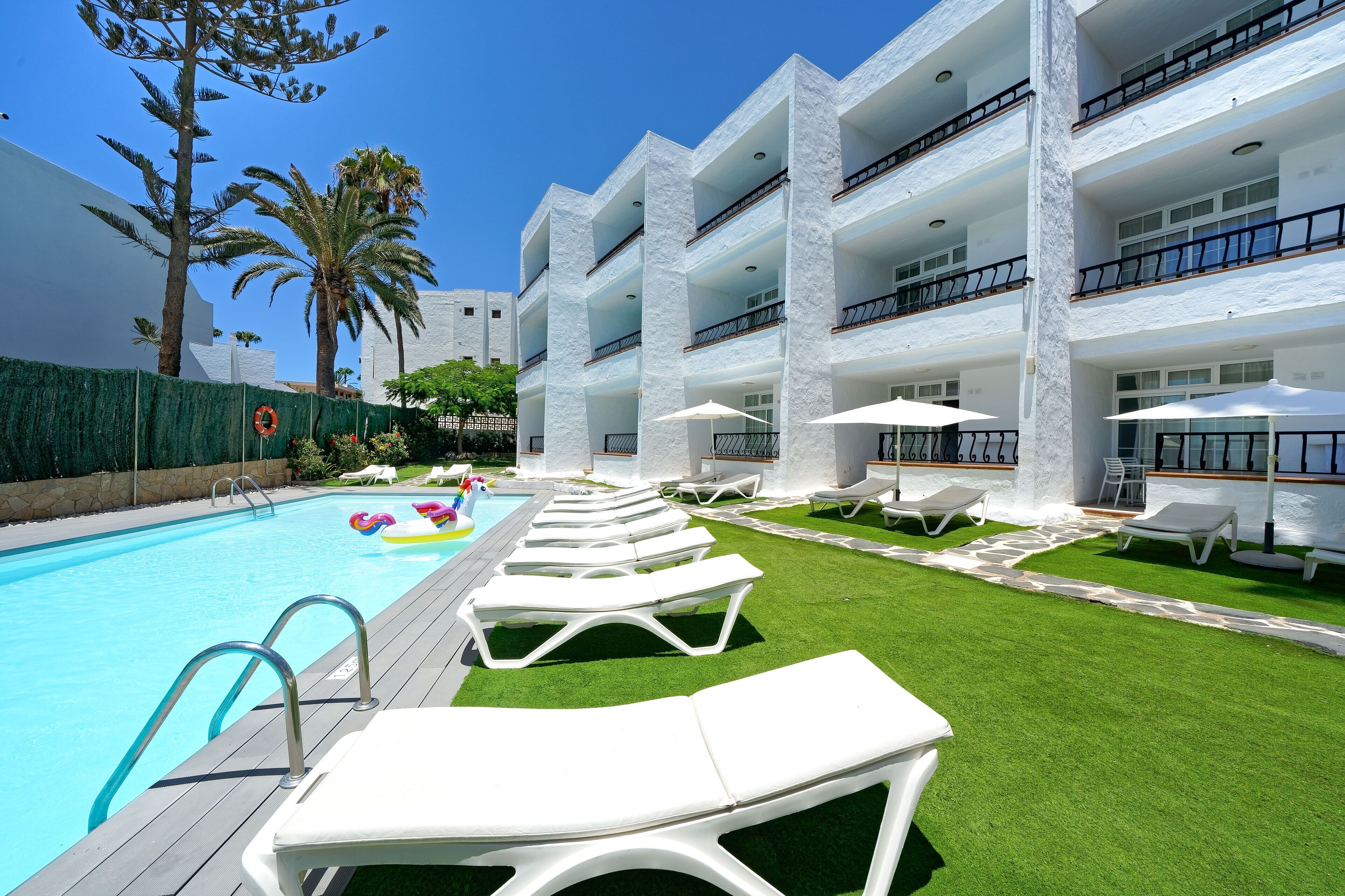 A pool area with white lounge chairs and umbrellas, surrounded by a well-maintained lawn and tall buildings.