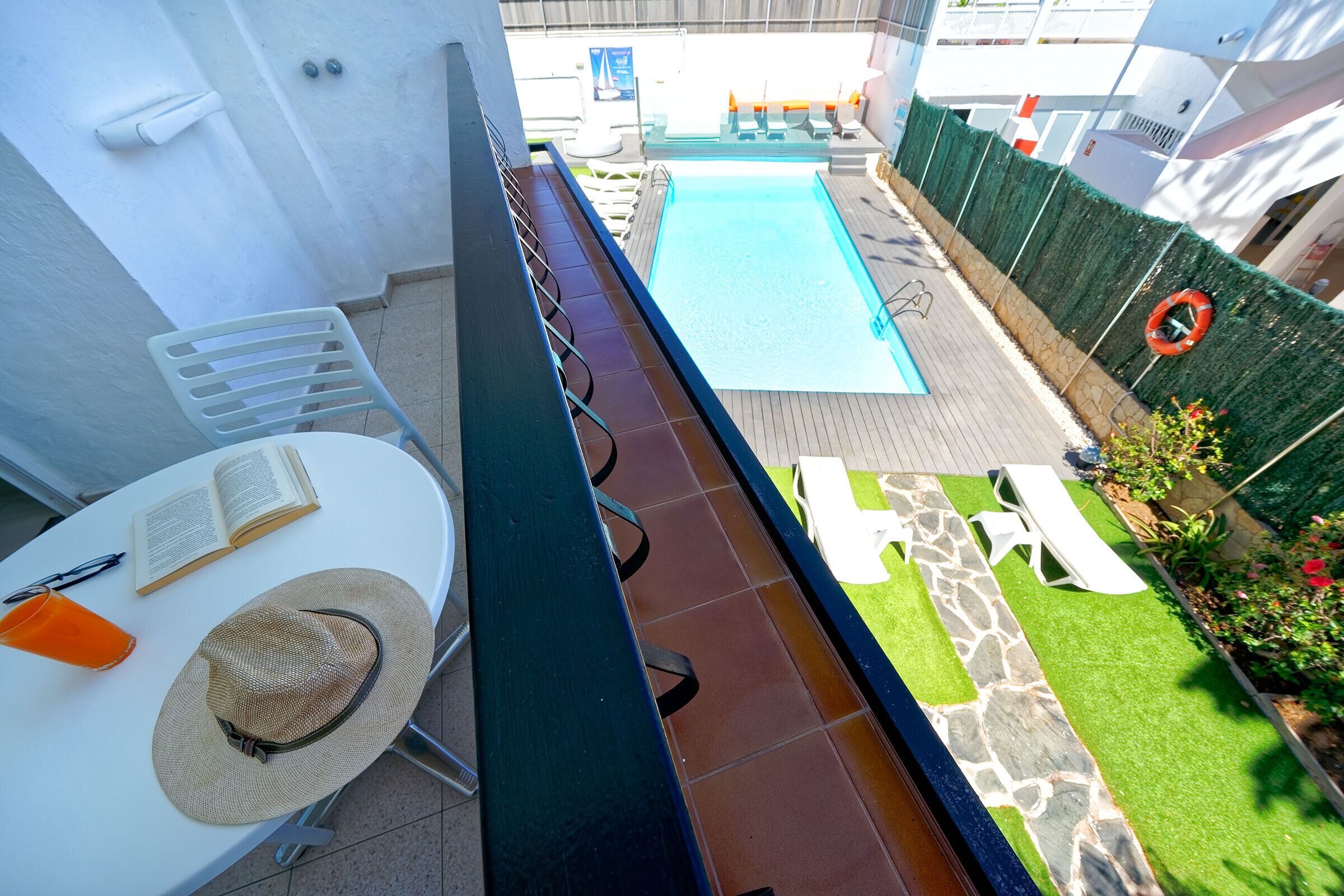 A rooftop pool area with a white table, a hat, and an open book.