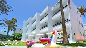 Un hotel con varios balcones, una zona de piscina con sillones de descanso y una gran decoración de unicornio inflable.