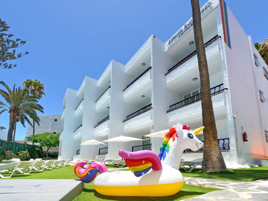 Un hôtel doté de nombreux balcons, d’un espace piscine avec des chaises longues et d’une grande décoration gonflable en forme de licorne.