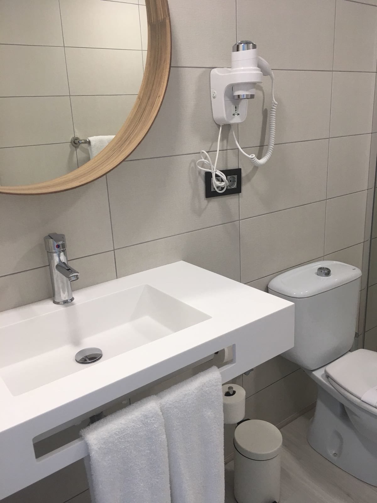 Kylpyhuone, jossa on valkoinen pesuallas, peili, wc-istuin ja roskakori.
