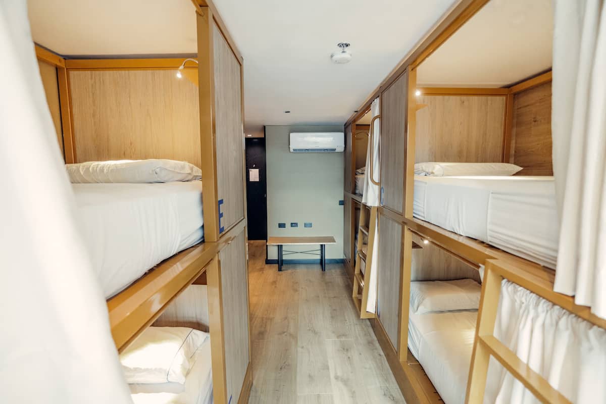 A narrow corridor with bunk beds on either side, a bench in the center, and an air conditioning unit on the wall.