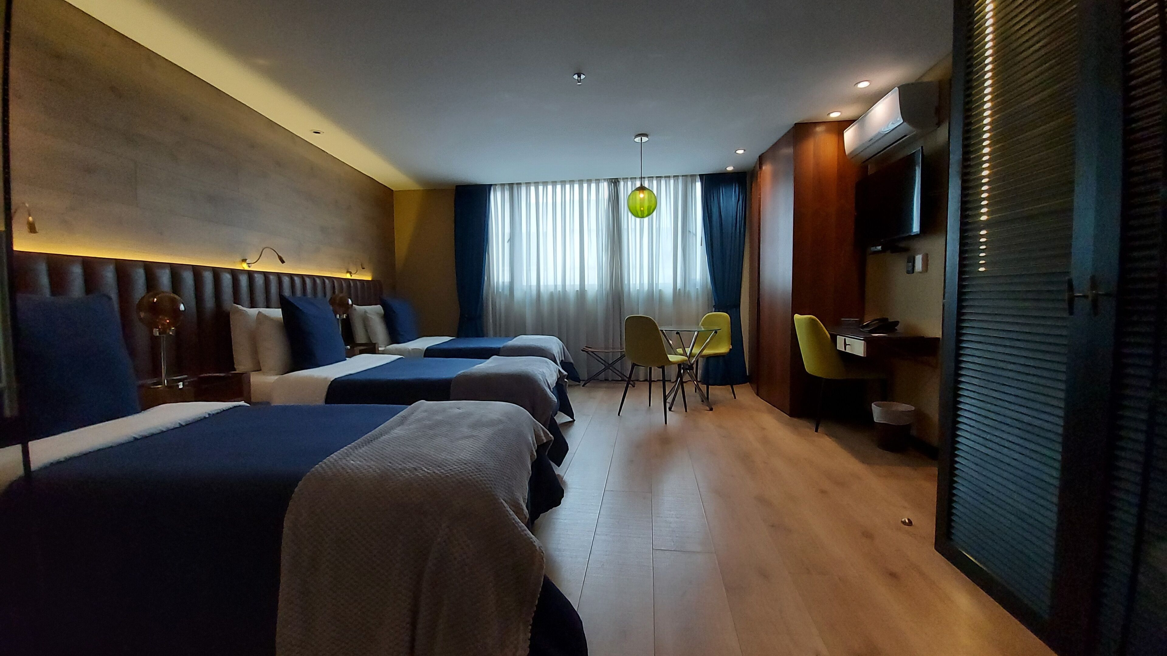 A hotel room with three beds, a desk, a chair, and a television.