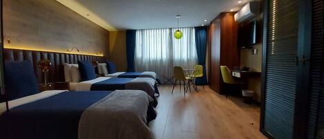 A hotel room with three beds, a desk, a chair, and a television.