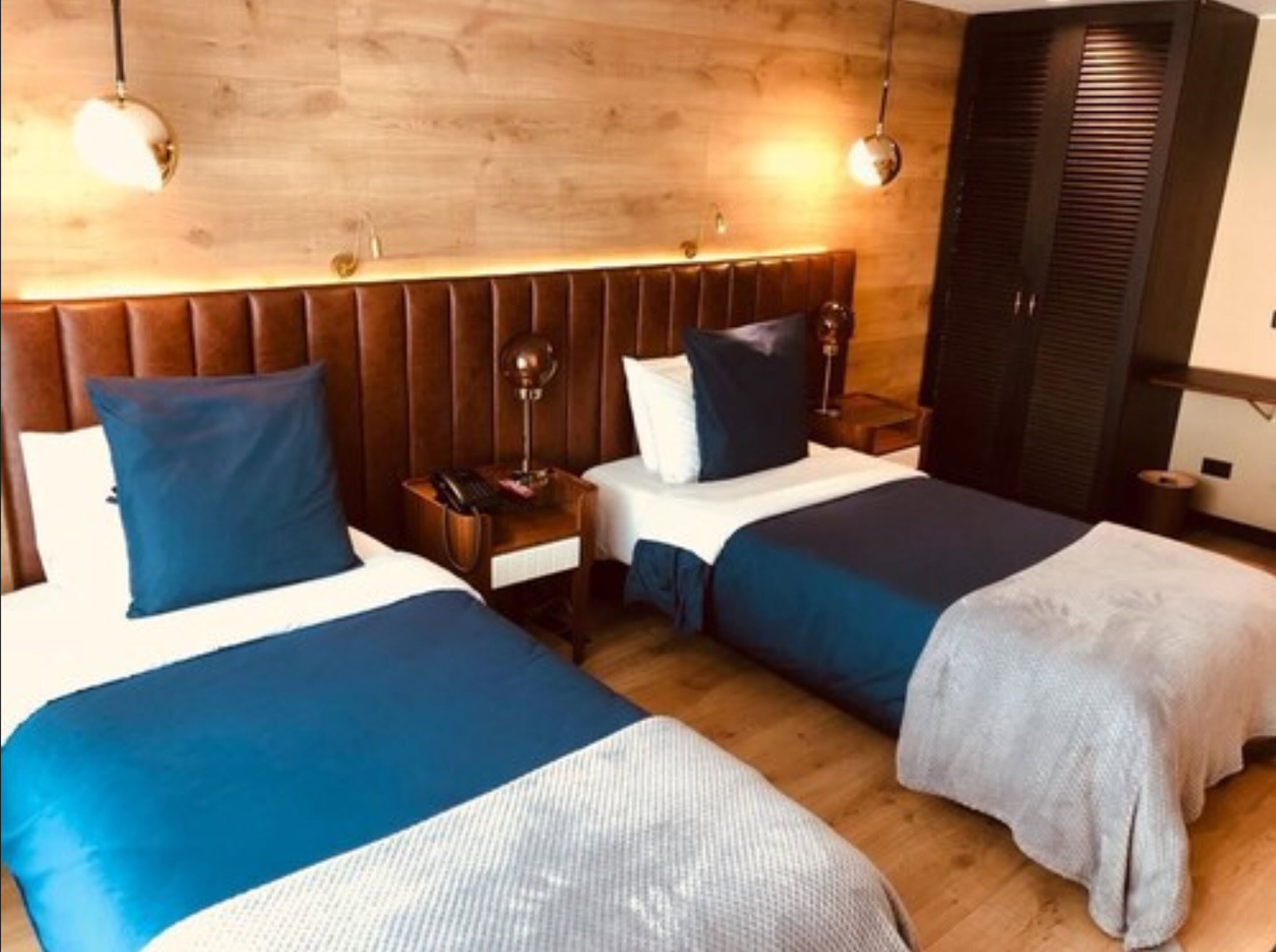 Habitación de hotel con dos camas, cabecero de madera, lámparas de noche y un armario.
