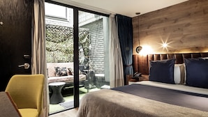 Un dormitorio con cama, una silla, una mesita de noche y vistas a un espacio exterior con sofá y plantas.