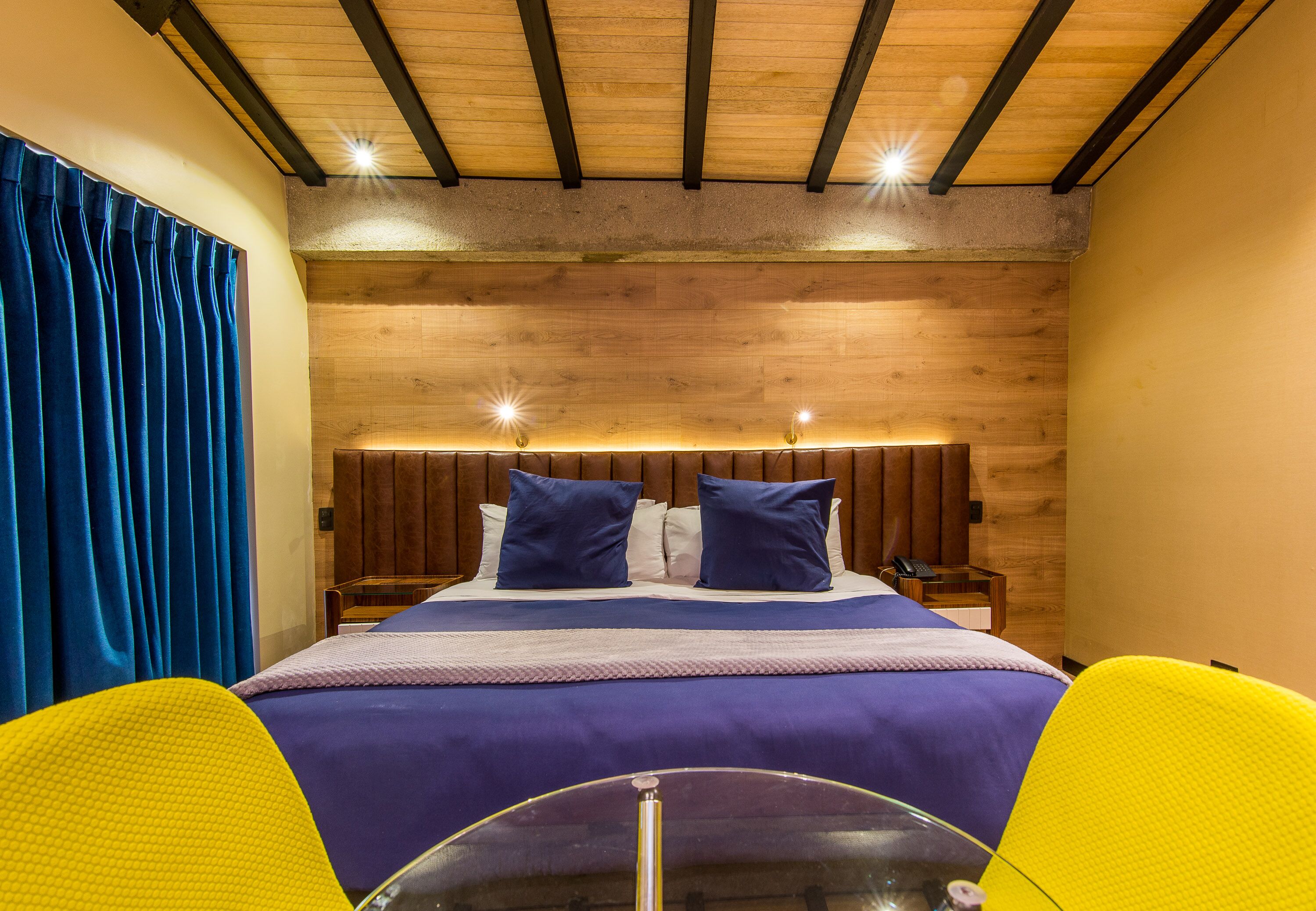 Una habitación de hotel con una cama grande, cabecero de madera y una mesa de vidrio al frente.