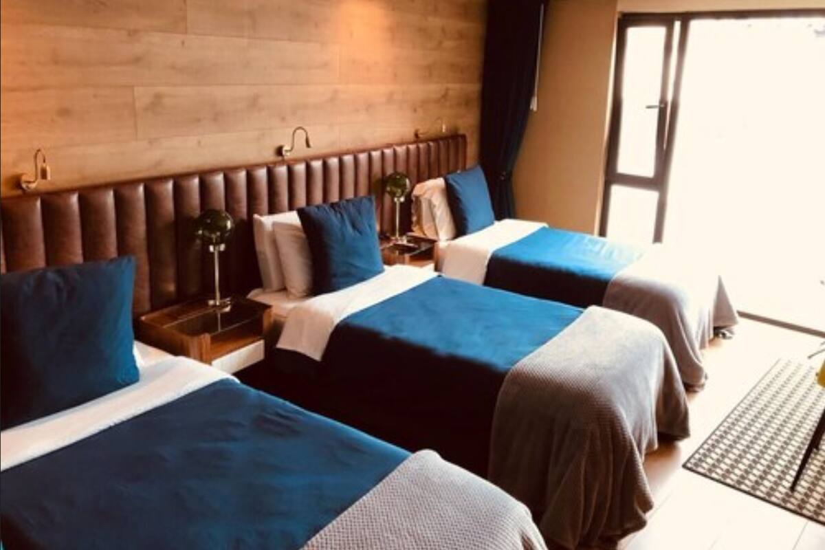 A hotel room with two beds, a wooden headboard, bedside lamps, and a view of the outdoors.