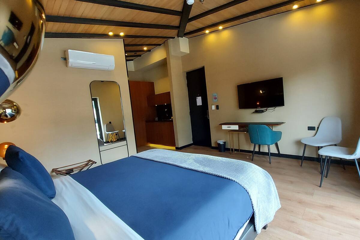 A modern hotel room with a bed, a desk, a TV, and a seating area.