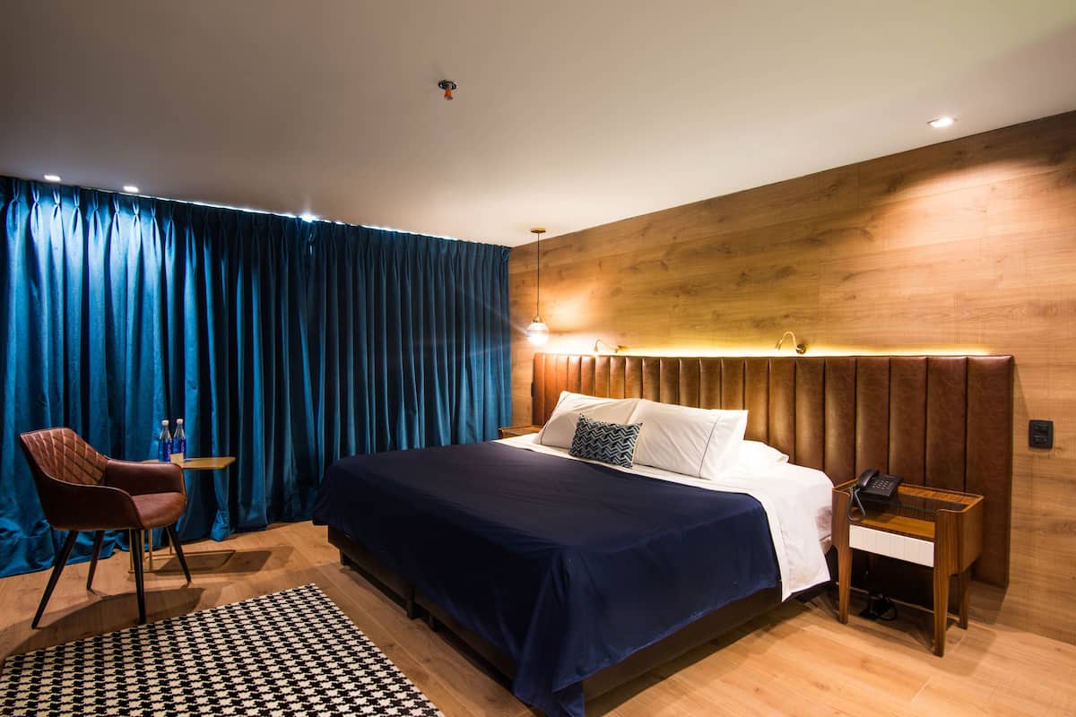 A modern hotel room with a large bed, a wooden headboard, a desk with a phone, and a chair.