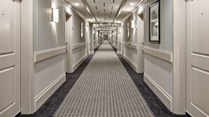 Un pasillo de hotel con alfombra estampada, cuadros en las paredes e iluminación empotrada en el techo.