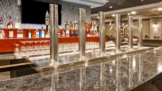 Zona de bar con encimera de granito, varios dispensadores de licor y una amplia variedad de botellas.