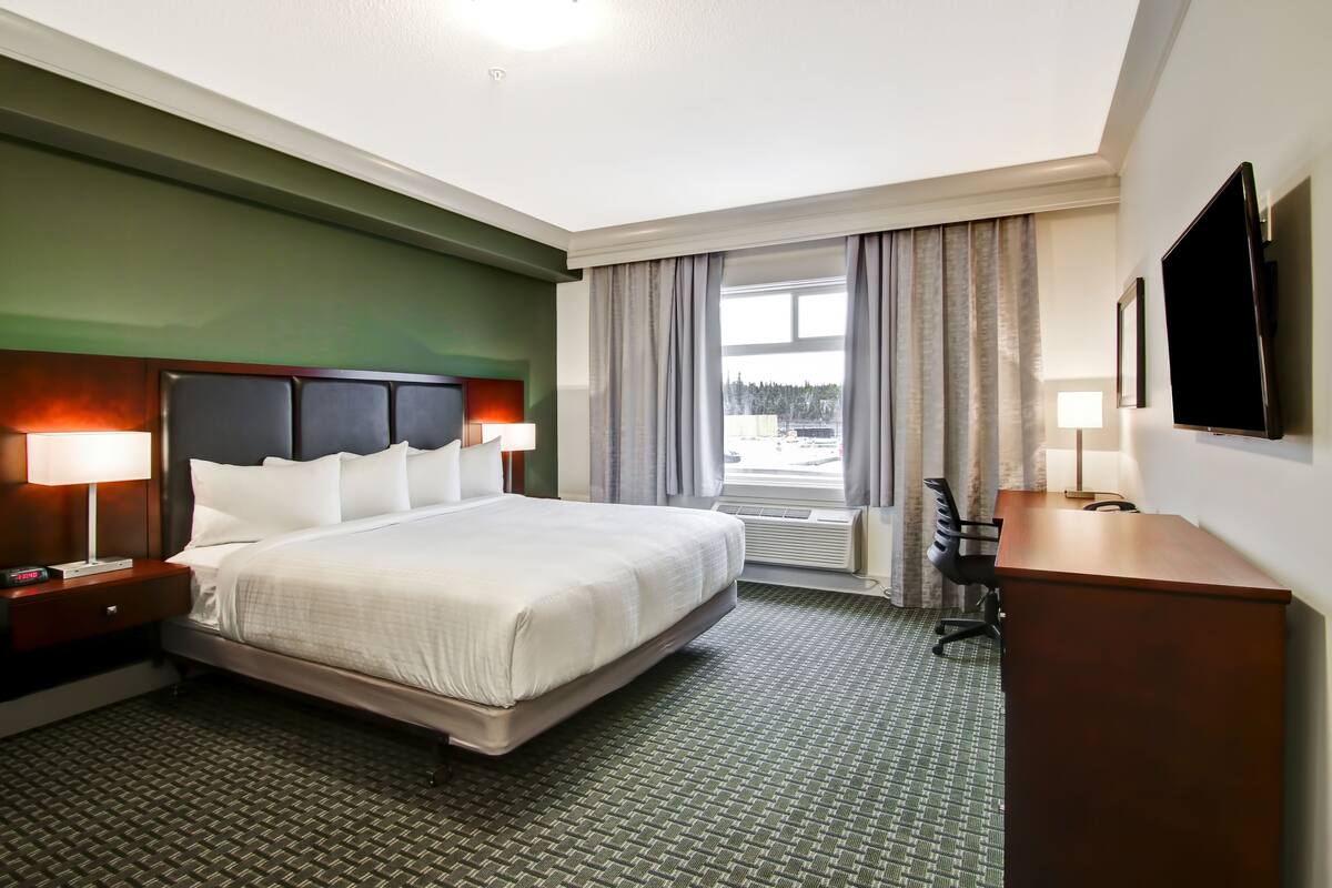 A hotel room with a large bed, bedside lamps, a desk, and a TV.