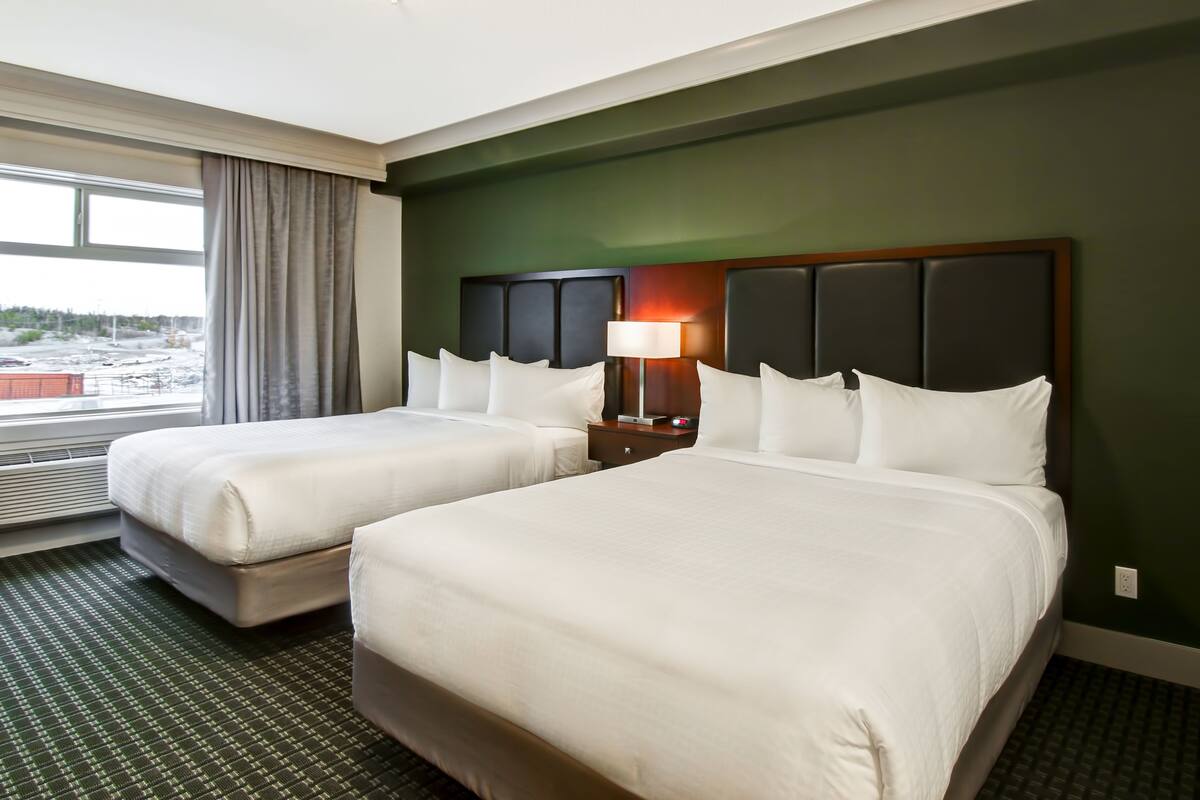 A hotel room with two beds, a nightstand with a lamp, and a view of a snowy landscape through the window.