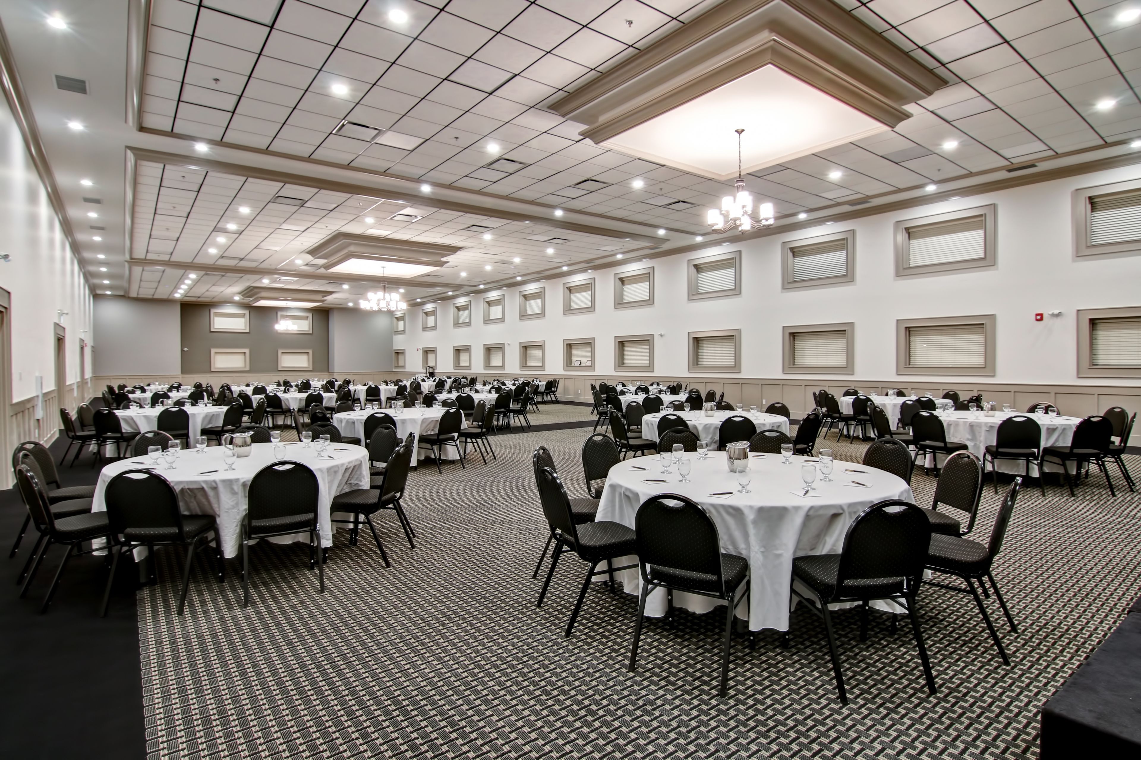 A large conference room with multiple round tables, each set with chairs and white tablecloths.