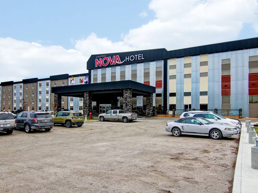 Um hotel com fachada moderna, entrada coberta e estacionamento com vários veículos.