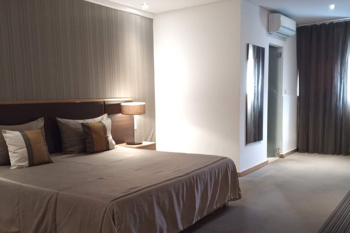 Habitación de hotel con una cama grande, cabecera, mesita de noche y unidad de aire acondicionado.