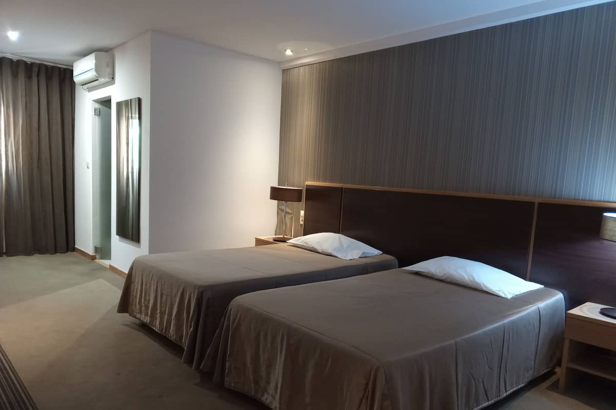 Una habitación de hotel con dos camas, un espejo grande, aire acondicionado de pared y una cortina.