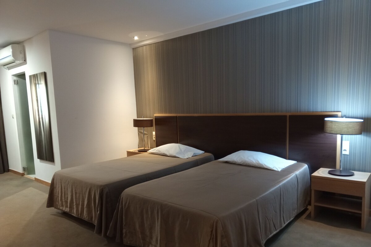 Ein Hotelzimmer mit zwei Betten, einem Holzkopfteil, Nachttischlampen und Teppichboden.