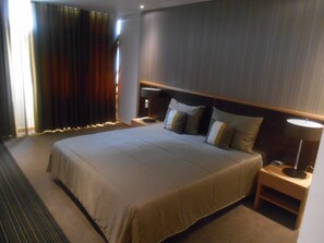 Une chambre d’hôtel avec un grand lit, une table de chevet avec une lampe et une fenêtre avec des rideaux.