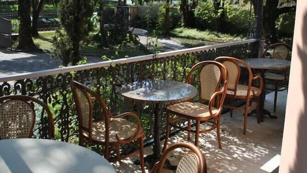 An outdoor seating area with wicker chairs and tables, surrounded by lush greenery and a view of the street. - Casablanca Koeler Hotel (Petrópolis)